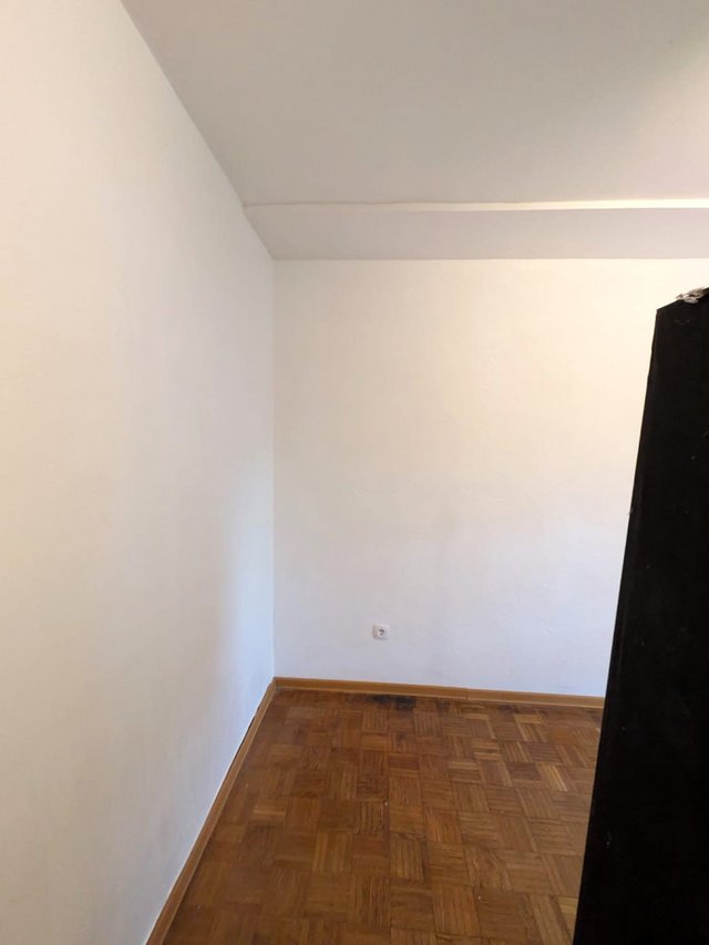 Leere Zimmerecke mit weißen Wänden, Parkettboden und Steckdose.