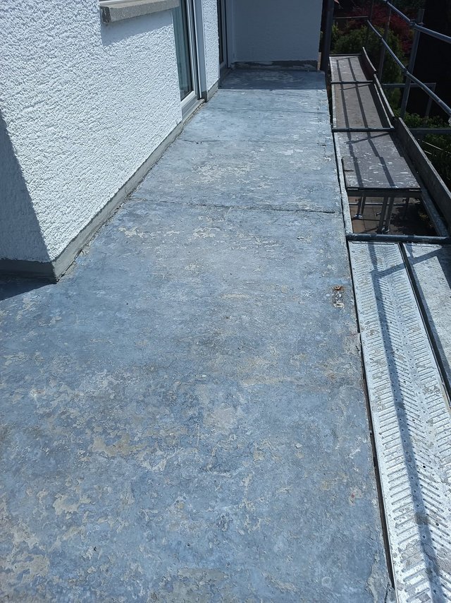 Grauer Balkonboden mit Abnutzungsspuren neben weißer Fassade und Metallgeländer