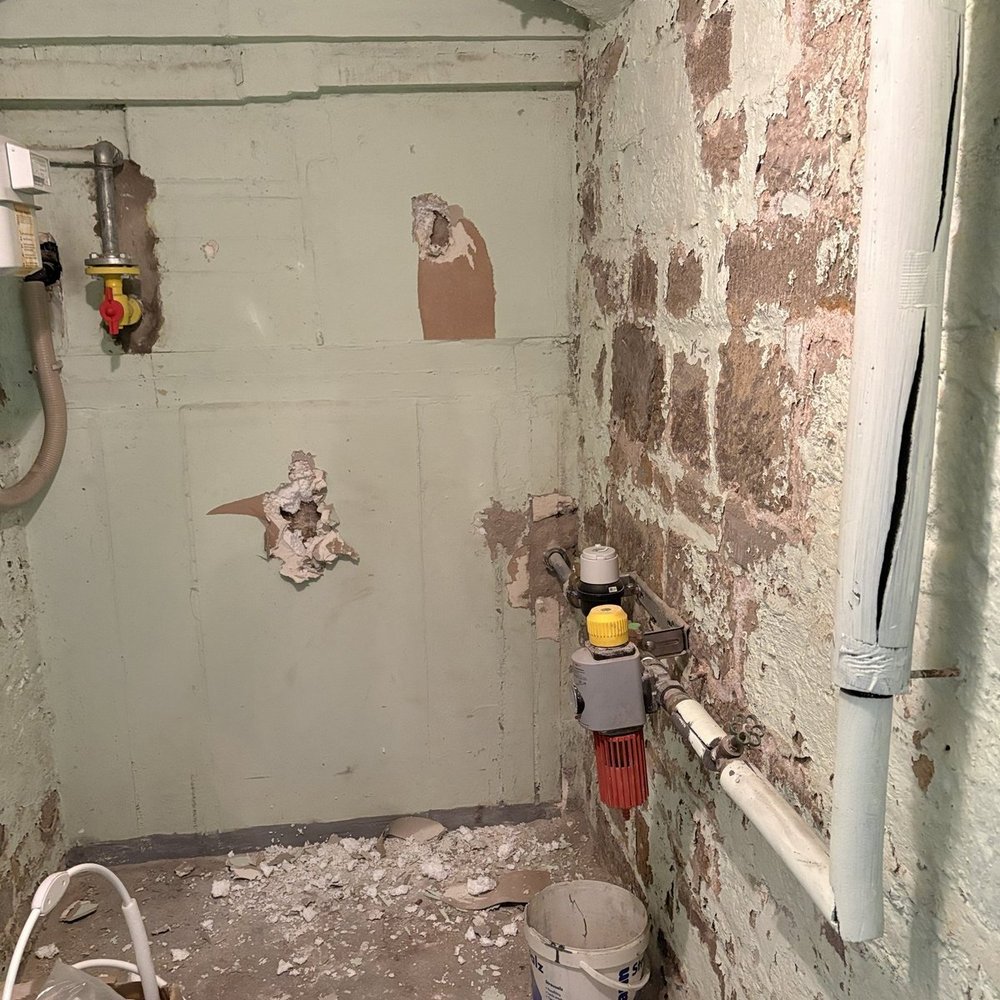 Abgeplatzter Putz und freiliegendes Mauerwerk in kleinem Kellerraum mit Rohrleitungen