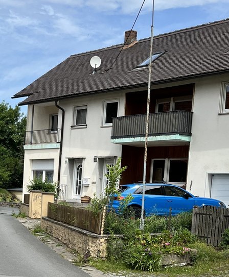 Wohnhaus mit zwei Balkonen und blauem Auto in der Einfahrt