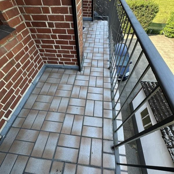 Balkon mit grauen Bodenfliesen, schwarzem Metallgeländer und roter Klinkerwand