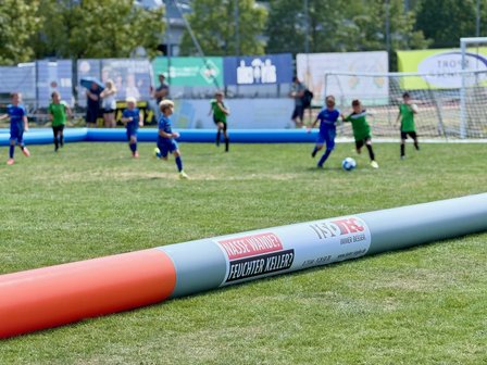 Kinder spielen Fußball auf Rasenplatz, Werbebande mit ISOTEC im Vordergrund
