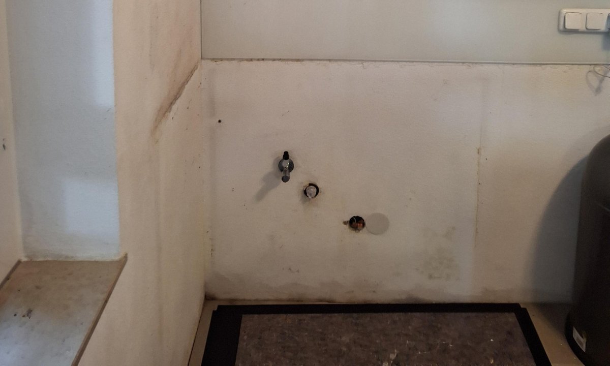 Küche mit verfärbter Wand, offenen Anschlüssen und Hängeschrank