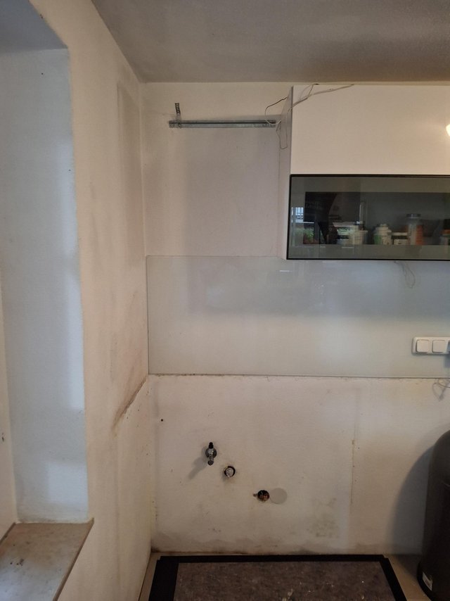 Küche mit verfärbter Wand, offenen Anschlüssen und Hängeschrank