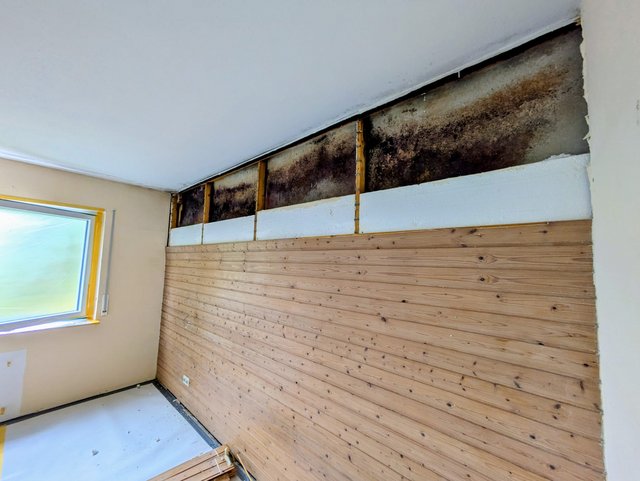 Geoeffnete Wandverkleidung zeigt dunkle Flecken an oberer Wandzone im Zimmer.