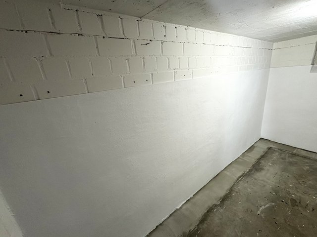 Weiß gestrichene Kellerwand aus Mauerwerk, Betonboden und Decke, Raumansicht