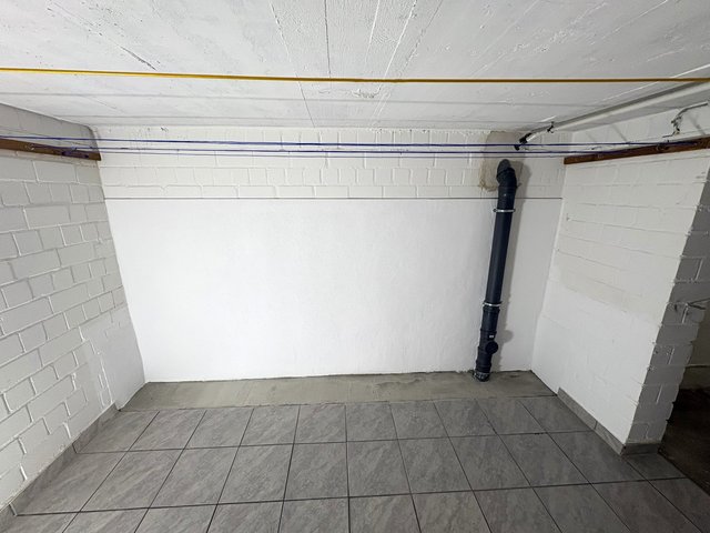 Weiß gestrichene Kellerwand mit schwarzem Abflussrohr und gefliestem Boden
