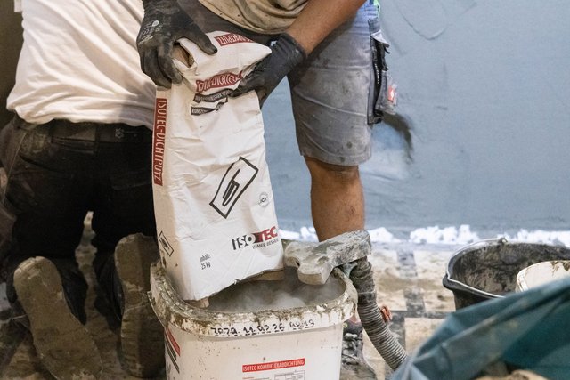 ISOTEC Mitarbeiter füllt graues Pulver aus Sack in Mischbehälter.