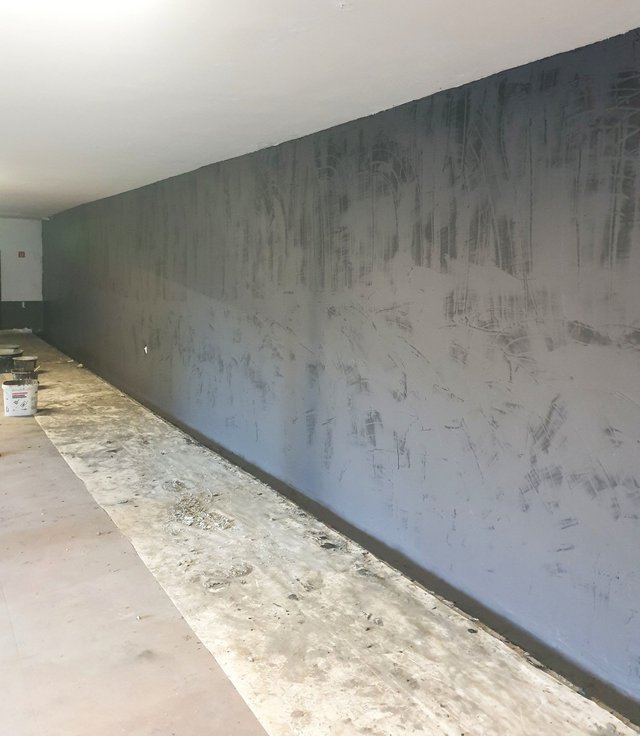 Schwarze Masse auf langer Zimmerwand aufgetragen, Renovierungsraum mit abgedecktem Boden