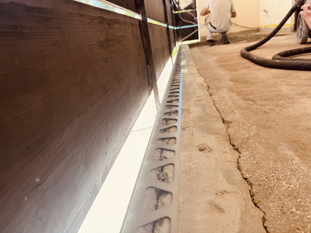 Arbeiter kniet neben Bodenrinne auf Betonboden mit Riss, Schlauch im Vordergrund