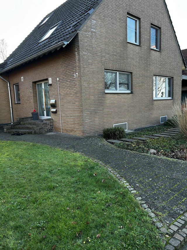 Ziegelhaus mit dunklem Satteldach, Eingangsbereich und gepflastertem Weg