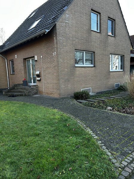 Ziegelhaus mit dunklem Satteldach, Eingangsbereich und gepflastertem Weg