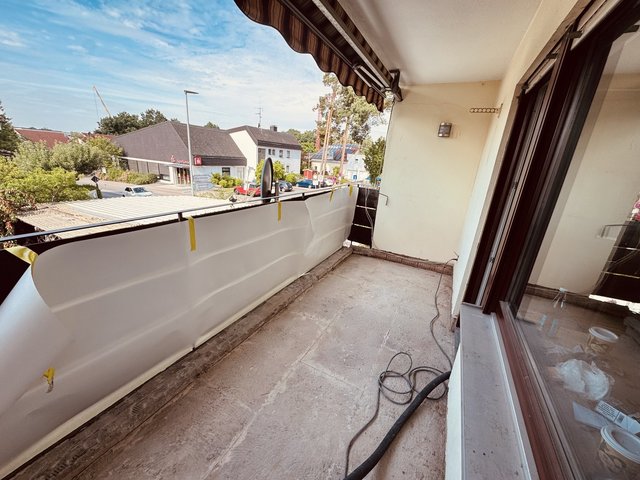 Balkon mit Abdeckfolie am Geländer, Kabel und Schlauch auf Betonboden, Blick auf Straße.