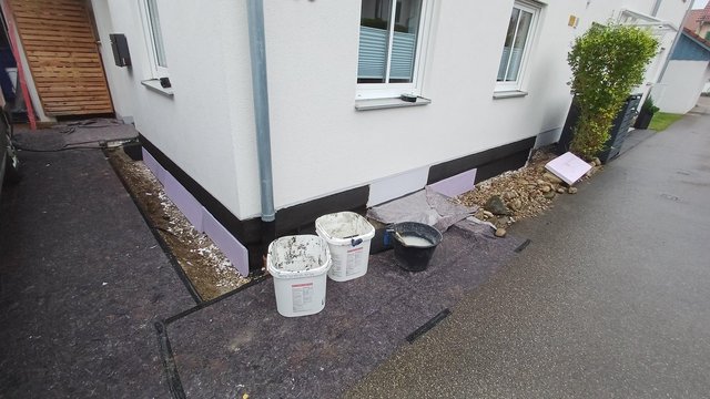 Schwarze Masse am Haussockel, helle Dämmplatten entlang der Gebäudeecke