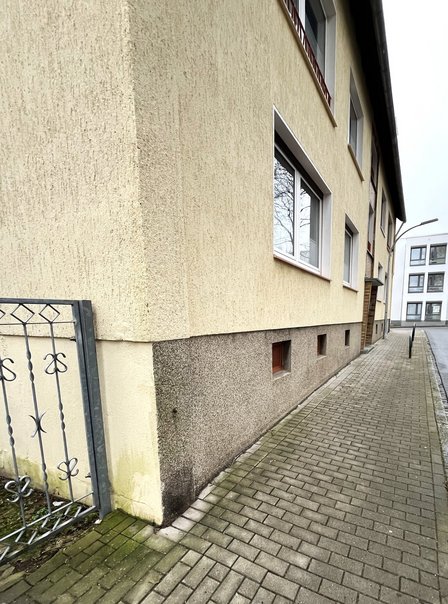 Hausfassade mit Sockelputz und Kellerfenstern am Gehweg, Perspektive entlang der Straße