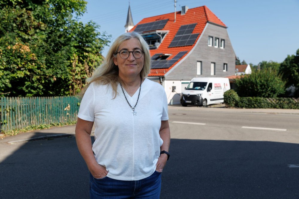 Frau mit Brille steht vor Haus mit Solarmodulen und weißem Transporter