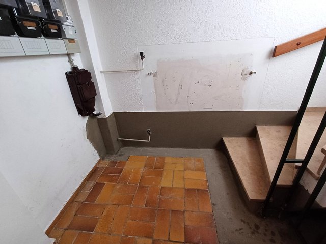 Treppenbereich mit grauer Abdichtung am Wandfuß und freiliegenden Rohranschlüssen