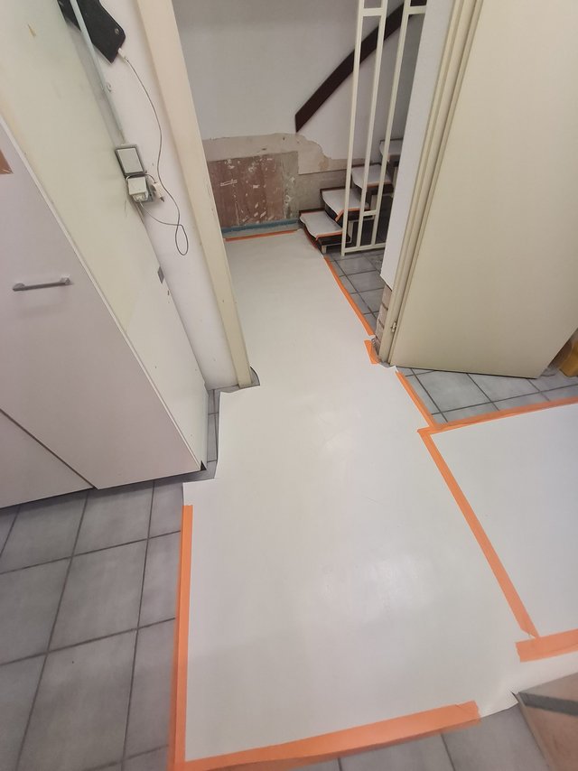 Abgeklebte Schutzfolie auf Fliesenboden im Treppenhaus, freigelegte Wandstelle