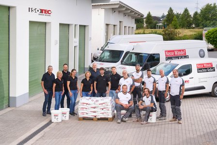 ISOTEC Teamfoto vor Firmengebäude mit Transportern, Materialpaletten und Eimern