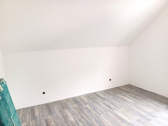 Leerer Raum mit weißer Wand, schräger Decke und grauem Bodenbelag