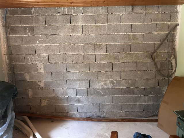 Graue Betonsteinwand mit hellen Ausblühungen und freiliegenden Kabeln im Raum