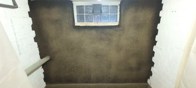 Dunkle beschichtete Kellerwand mit kleinem Glasbausteinfenster