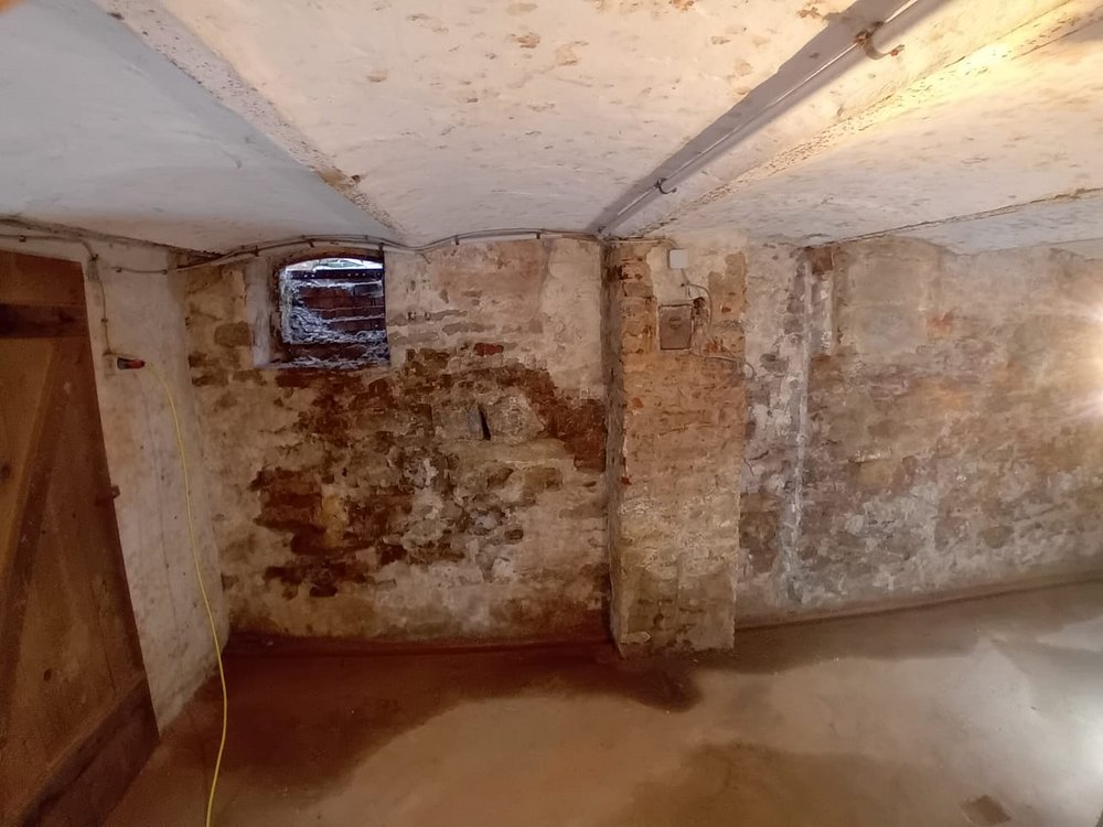 Feuchte Kellerwand aus Mauerwerk mit abplatzendem Putz und kleinem Fenster