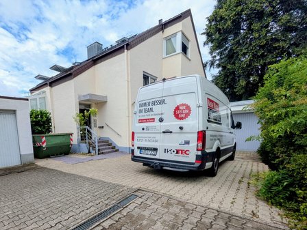 ISOTEC Transporter steht vor Wohnhaus im Hof neben Garage und Grüncontainer.
