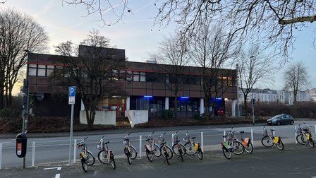 Fahrradstation mit Leihfahrrädern vor Bürogebäude an Straßenrand, Bäume im Abendlicht
