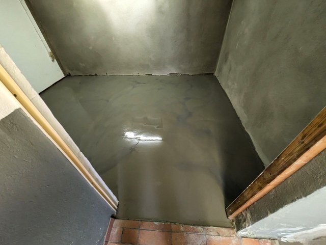 Glänzender grauer Bodenbelag in kleinem Raum, Blick in eine Ecke.