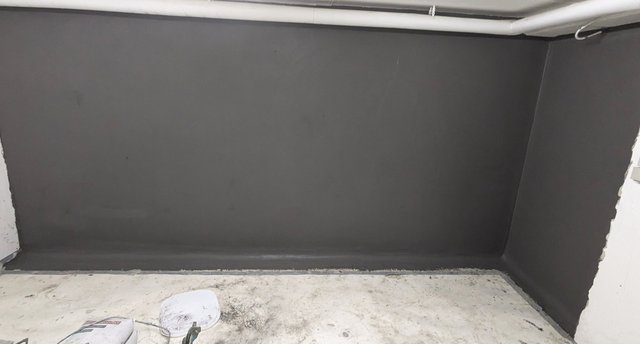 Kellerraum mit dunkelgrau beschichteter Wand, Boden mit Werkzeug und Schmutzspuren.