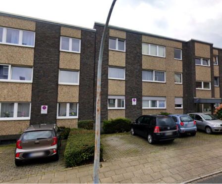 Mehrfamilienhausfassade mit Fensterreihen, parkenden Autos und Straßenlaterne im Vordergrund