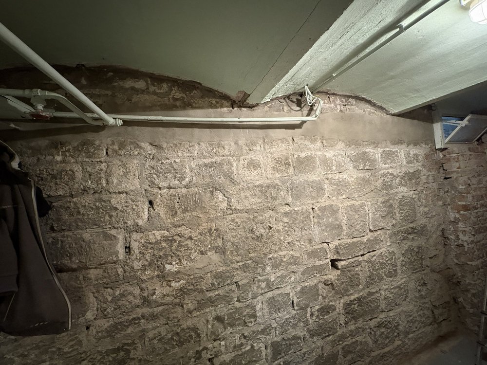 Freigelegte Kellerwand aus Naturstein mit Rissen und Leitungen unter der Decke
