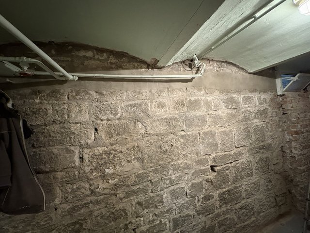 Freigelegte Kellerwand aus Naturstein mit Rissen und Leitungen unter der Decke