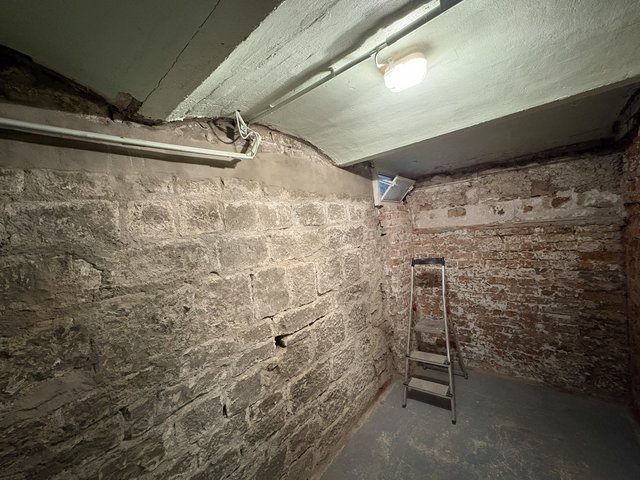 Kellerraum mit freigelegten Stein- und Ziegelwänden, Leiter und Deckenbeleuchtung