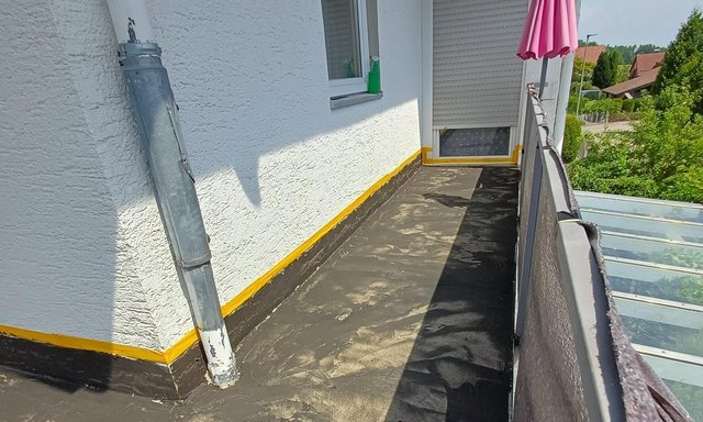 Balkon mit schwarzer Beschichtung, Fallrohr, Fenster und pinkem Sonnenschirm