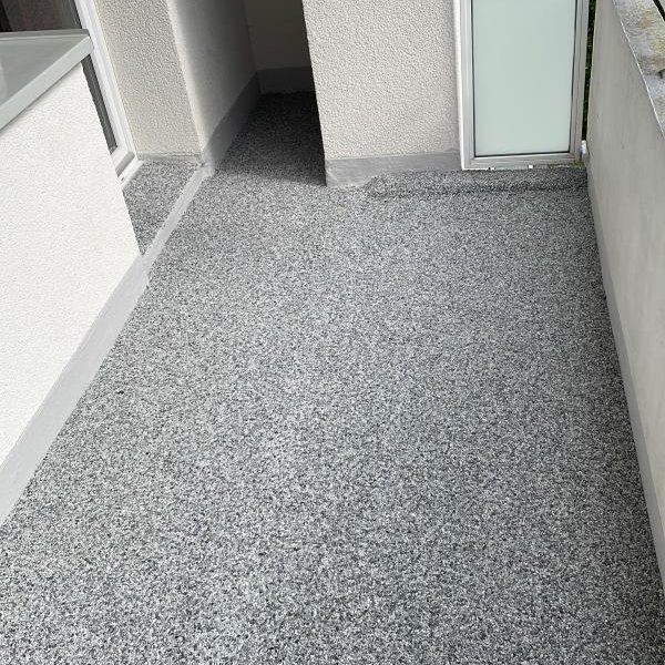 Balkon mit grauem, steinähnlichem Bodenbelag und weißem Geländer