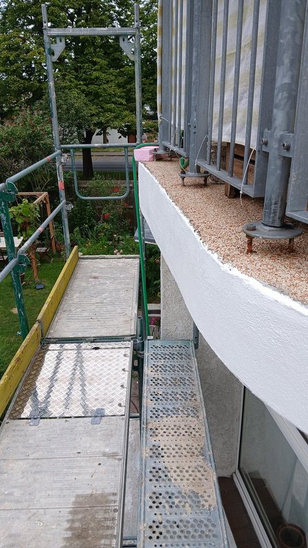 Gerüst am Balkonrand mit Kiesbelag und Metallgeländer, Blick nach unten.