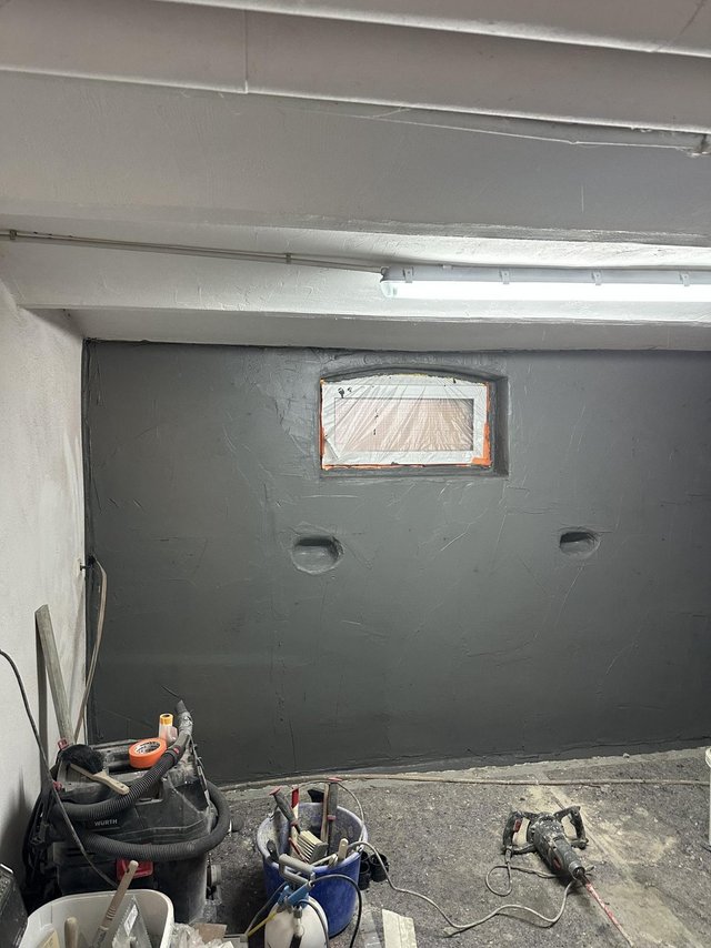 Kellerraum mit grauer Masse beschichteter Wand, abgeklebtes Fenster, Werkzeuge am Boden