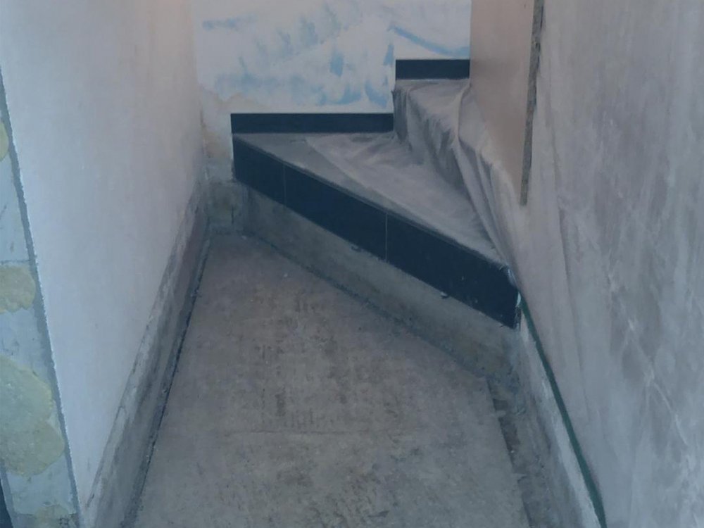 Schmaler Flur mit freigelegtem Betonboden und abgeklebten Wandkanten.