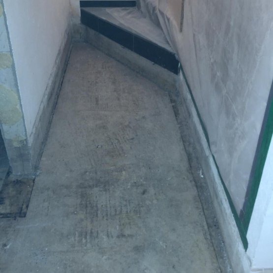 Schmaler Flur mit freigelegtem Betonboden und abgeklebten Wandkanten.