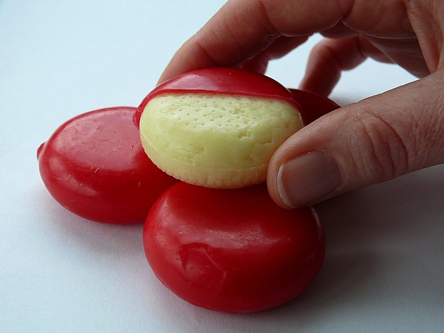 Hand entfernt rote Wachsschicht von rundem Käse