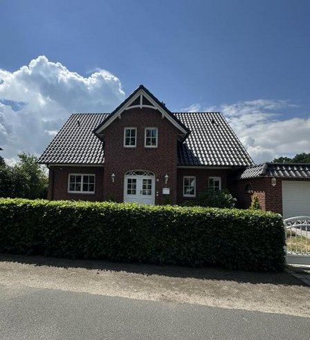Backsteinhaus mit Satteldach, Hecke und Garage an einer Straße