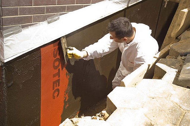 ISOTEC Mitarbeiter trägt dunkle Masse auf Kellerwand auf.