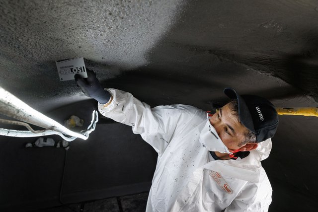 ISOTEC Mitarbeiter glättet schwarze Masse an Decke mit Spachtel.