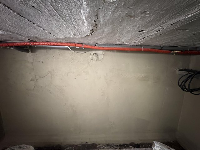 Rissige Betondecke mit Rohrleitungen über verputzter Kellerwand