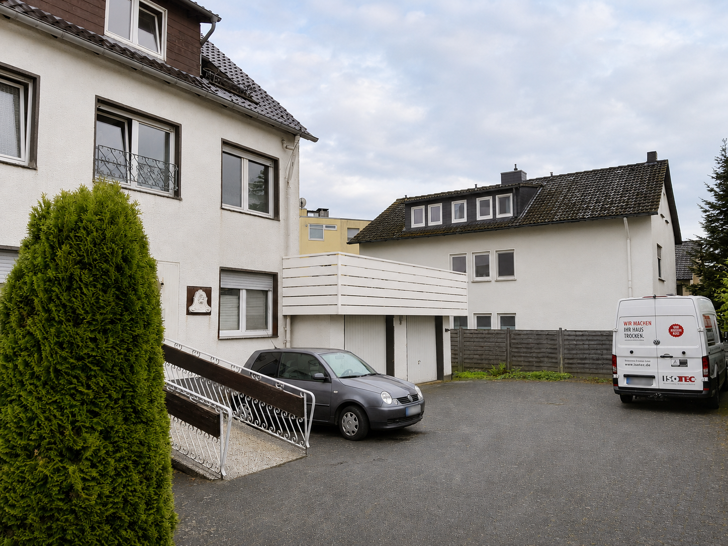 ISOTEC Transporter steht auf Hof vor Wohnhaus mit Balkon und Garage.