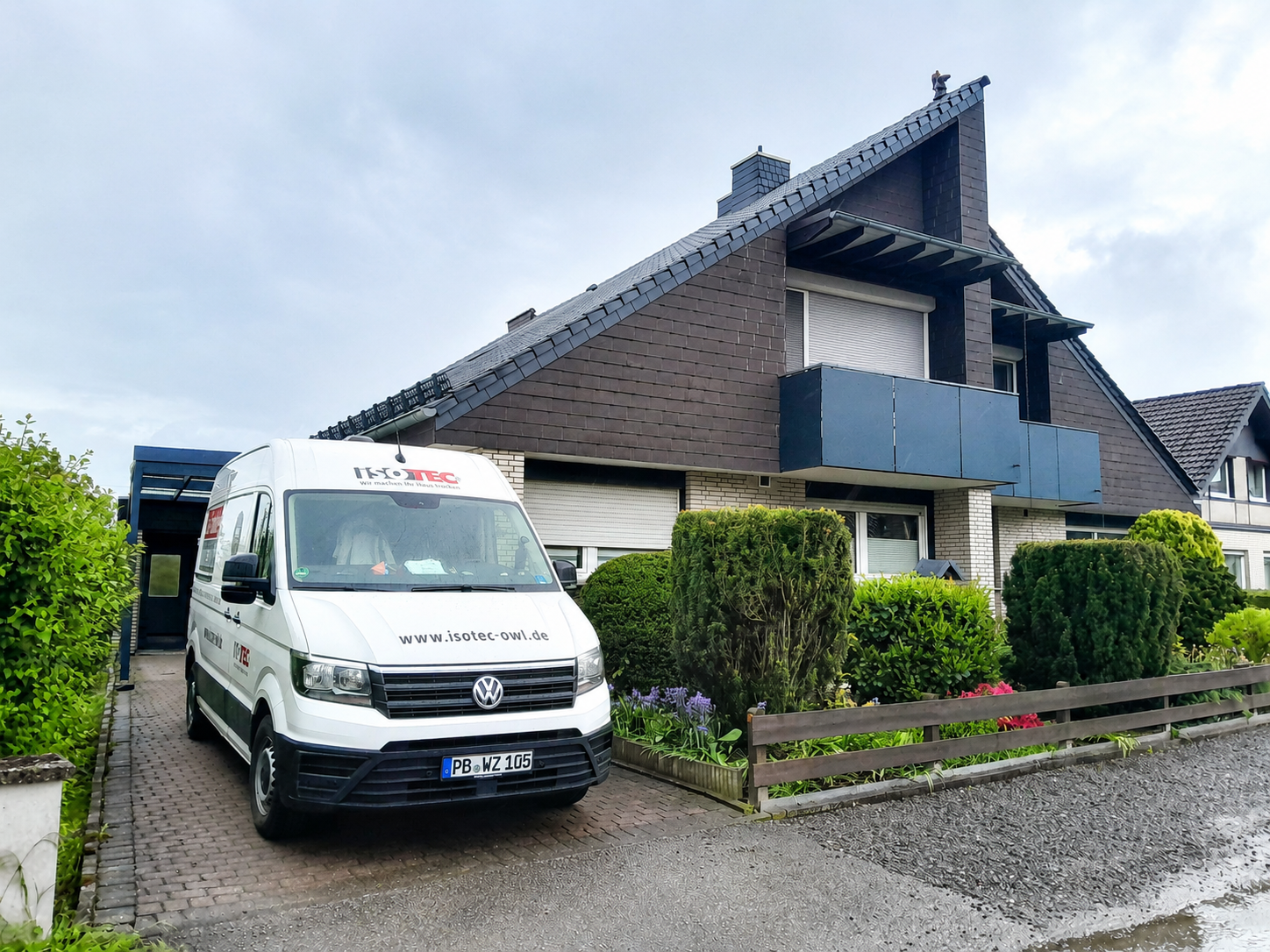 ISOTEC Transporter steht vor Einfamilienhaus mit Balkon und Garten.