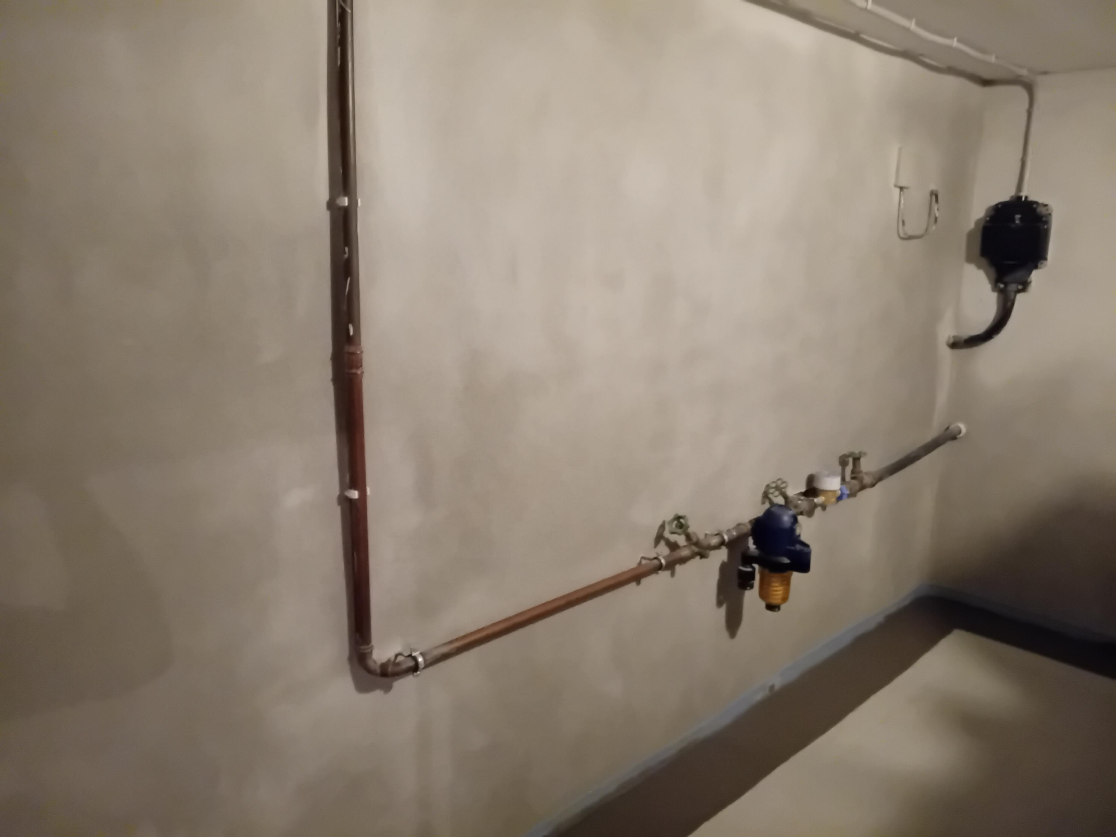Graue Kellerwand mit Rohrleitungen, Ventilen und Wasserfilteranlage