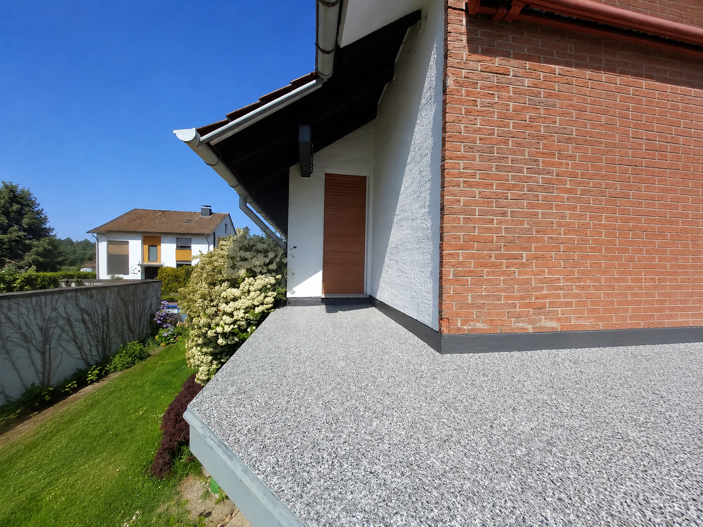 Balkon mit grauem Belag, Ziegelwand, Dachrinne und Tür, Gartenblick